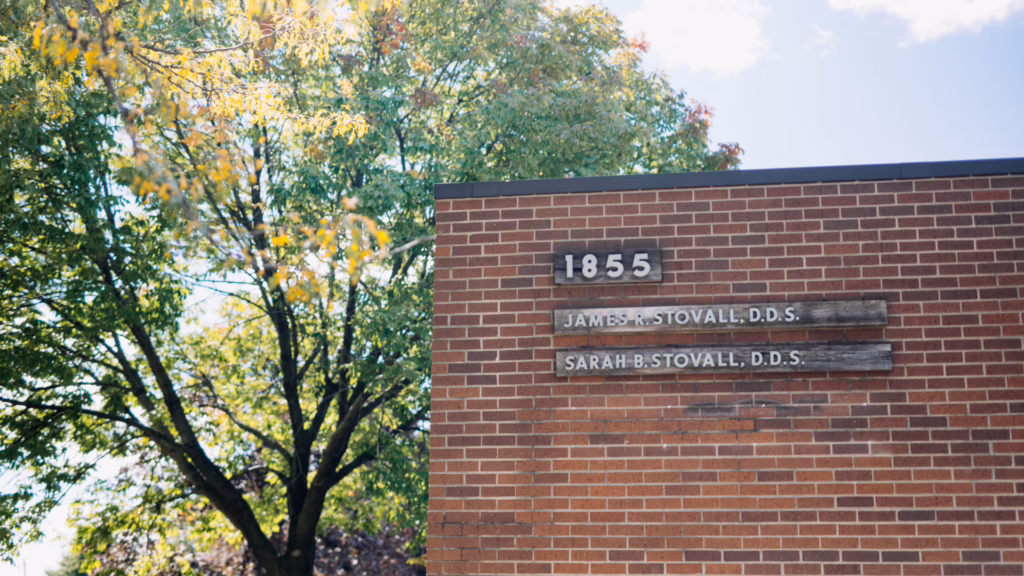 Brick building exterior showing the number 1855 and two weathered plaques with the names James R. Stovall, D.D.S., and Sarah B. Stovall, D.D.S., with trees in the background