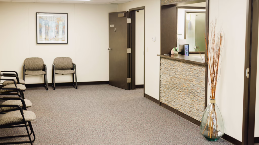 Waiting area with beige chairs along the left wall, framed forest print, and a reception desk on the right.