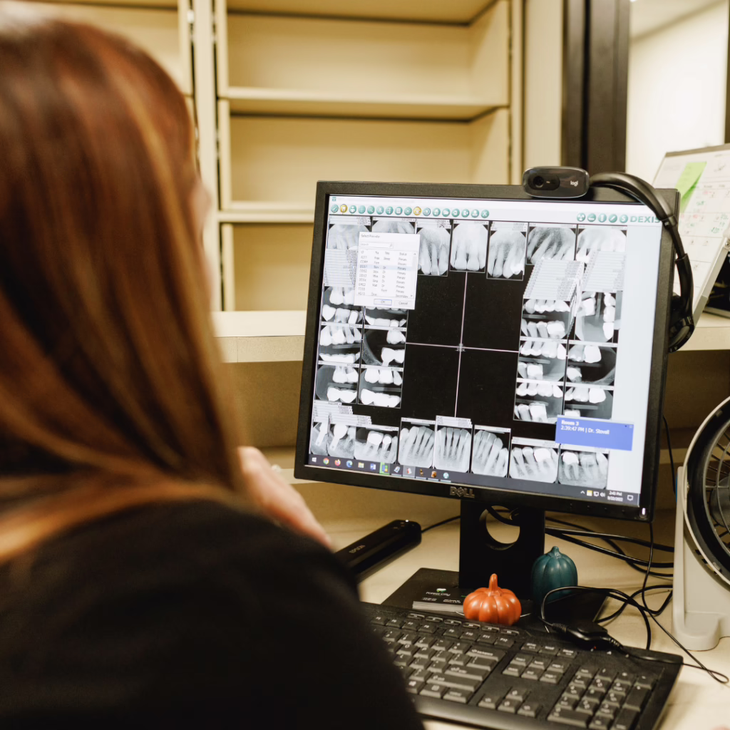 Dental X-ray images displayed on a computer monitor as a clinician reviews them at a desk.