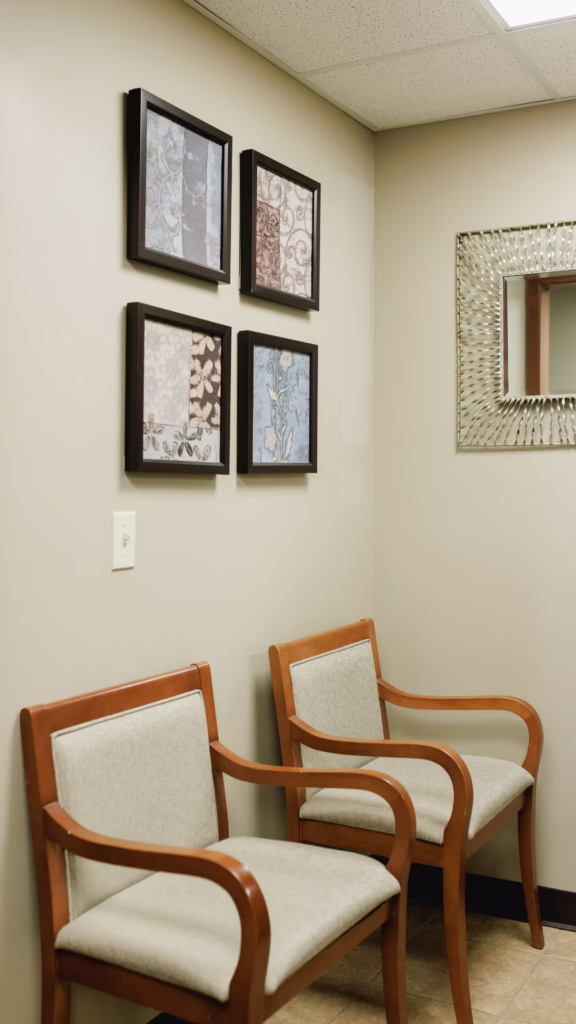 Waiting area with four framed fabric-pattern artworks on a beige wall and wooden chairs nearby.